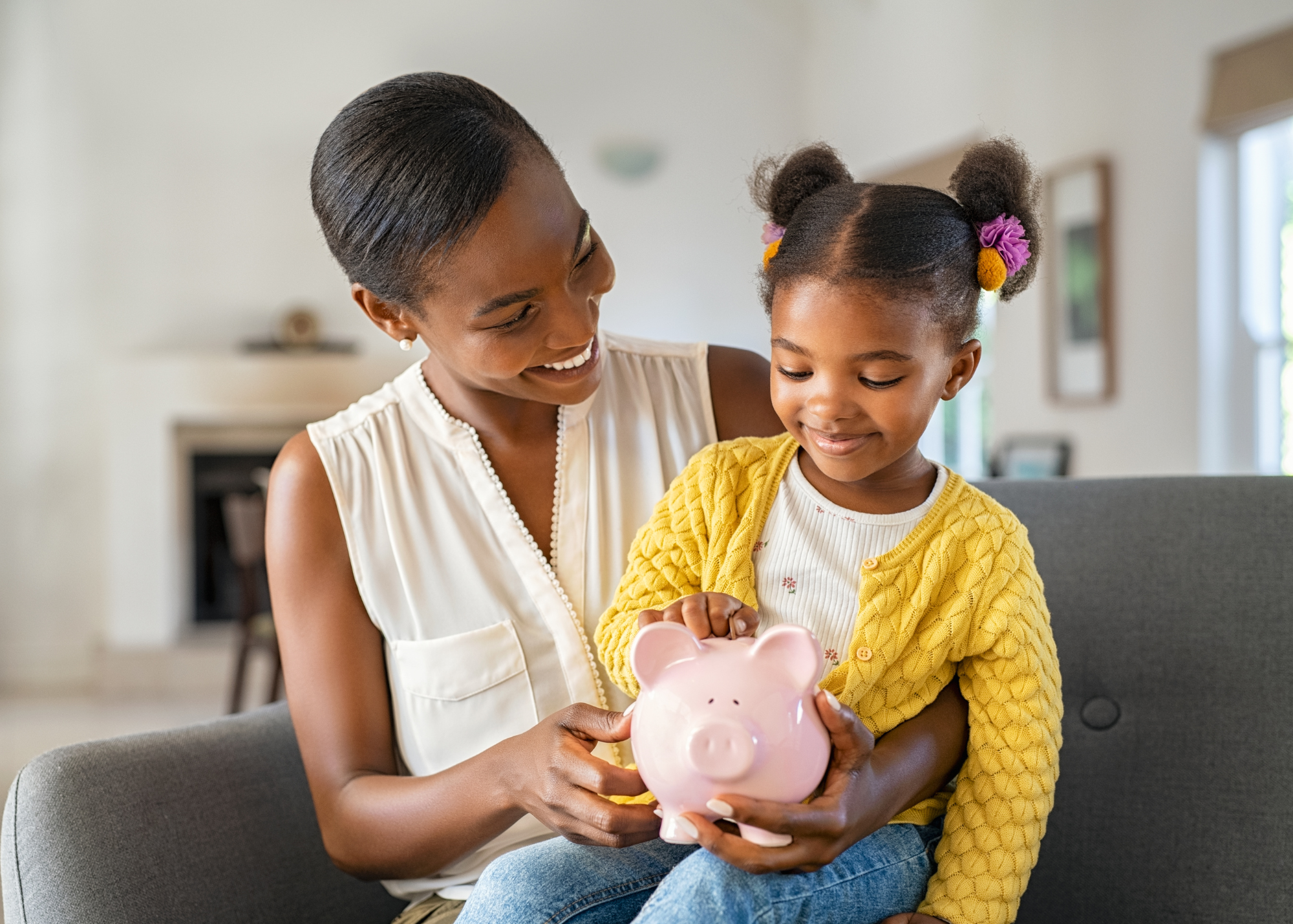 Black mom and daughter putting money into a piggy bank.